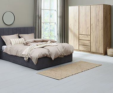 Chambre à coucher composée d'une grande armoire en bois et d'un lit double en tissu gris foncé