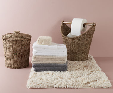 Flauschiger Badeteppich in Beige, darauf Handtücher in diversen Farben und zwei Körbe im geflochten Stil
