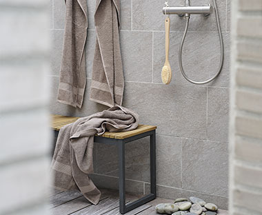 Asciugamani beige appese e appoggiate su una panca davanti alla doccia