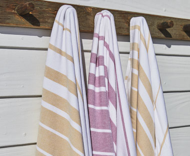 Drei Strandtücher in weiss-rosa und weiss-gelb hangen an je einem Haken draussen