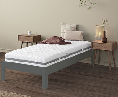 Camera da letto con un materasso a molle singolo GOLD S25 su una struttura letto grigia, con due comodini