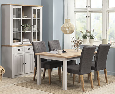 Salle à manger avec du mobilier moderne comprenant un buffet blanc, une table couleur chêne/blanc et quatre chaises en tissu gris