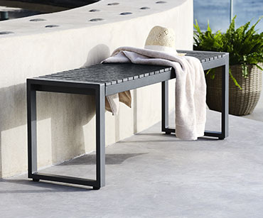 Schwarze Sitzbank aus Kunstholz und Stahl, darauf ein helles Handtuch