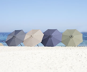 Vier verschiedenfarbige Sonnenschirme an einem Strand nebeneinander aufgereiht 