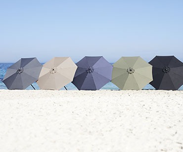 Vier verschiedenfarbige Sonnenschirme an einem Strand nebeneinander aufgereiht