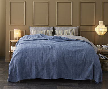 Dunkelblaue Tagesdecke auf einem Bett mit grauen und farbig gestreiften Kopfkissen