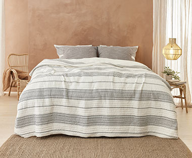 Chambre à coucher de style ethnique avec chaises et tabouret en rotin naturel et couvre-lit rayé gris et beige