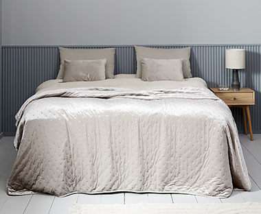 Chambre à coucher traditionnelle avec lit, draps et murs gris et objets décoratifs en bois soigneusement disposés sur la table de chevet bleu clair