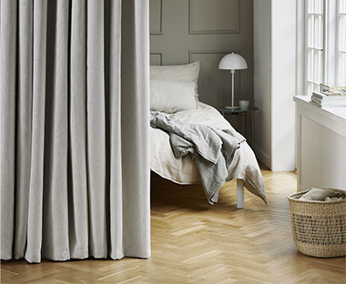 Chambre à coucher avec lit et murs clairs, et avec rideau de séparation en gris