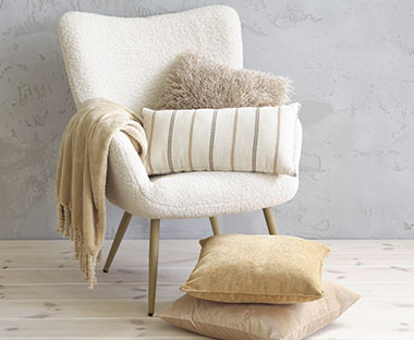 Pièce claire avec un fauteuil en velours blanc avec des coussins et un édredon sur le fauteuil et sur le sol