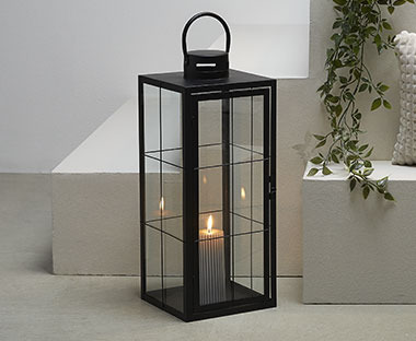 Lanterna nera moderna con candela affiancata da pianta cadente