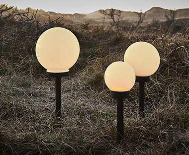 3 lampes solaires de formes rondes de différents tailles posées dans un jardin