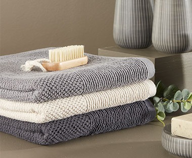 Asciugamani nei colori grigio chiaro, grigio scuro e in bianco, appoggiata su di esse una spazzola per igiene unghie