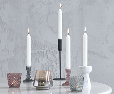 Diversi candelieri e portacandeline di coliri e materiali diversi, posti su un tavolo tondo bianco