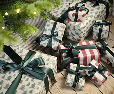 Pacchetti regalo natalizi incartati con la carta da regalo KARDUS posti sotto un albero di Natale