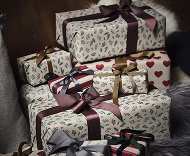 De nombreux cadeaux de Noël emballés dans du beau papier cadeau et présentés avec un nœud violet