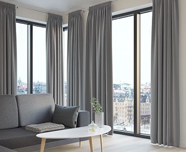 Wohnzimmer mit einem grauen Sofa, einem weissen Couchtisch und samtigen Vorhängen in Grau