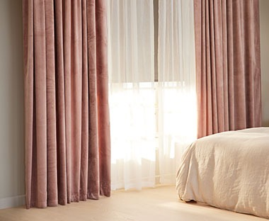 Schlafzimmer mit einem halbtransparenten Vorhang in Weiss, davor ein schwerer Vorhang in Altrosa