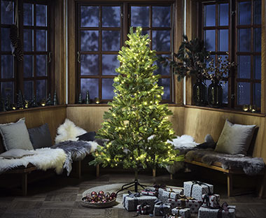 Künstlicher grüner Weihnachtsbaum mit leuchtendem Baumschmuck, darunter viele Geschenke