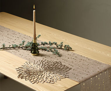 Holztisch mit beige-goldenem Tischläufer, Kerzenhalter, Tischset und Tannenzweig dekoriert