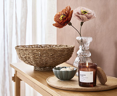 Eine Vase mit Kunstblumen, Schalen und eine Duftkerze auf einem Holzregal