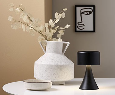 Vase aus Keramik mit Kunstblume neben einer schwarzen Dekoleuchte aufgestellt