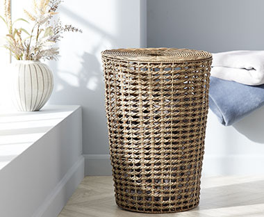 Ein runder Wäschekorb aus Polyethylen und eine runde, gestreifte Vase mit  Kunstblumen