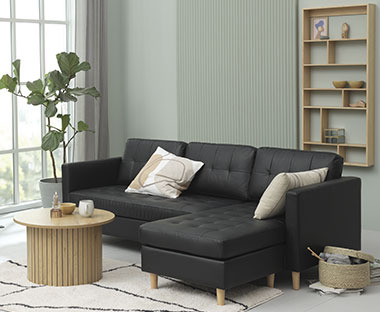 Grand canapé avec méridienne en simili cuir noir devant une jolie table basse ronde en bois
