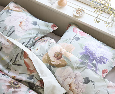 Un parure de lit aux motifs floraux recouvre un lit sous une fenêtre lumineuse