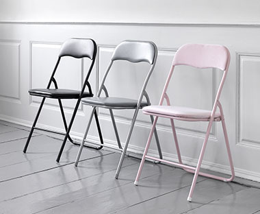 Tre sedie pieghevoli in nero, grigio e rosa disposte una accanto all'altro in una stanza luminosa