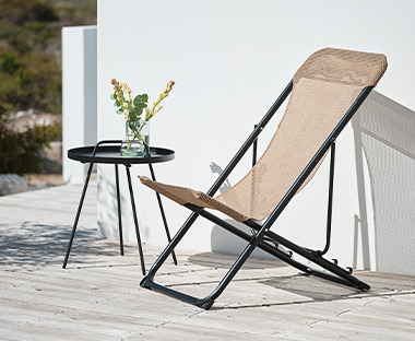 Chaise de jardin empilable en tissu beige et métal noir placée sur la terrasse à côté de la table basse