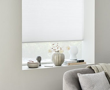 Store occultant plissé blanc accroché à la fenêtre, avec appui de fenêtre décoratif