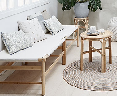 Panca minimalista e chic in legno con cuscini  davanti a uno sgabello in rattan naturale
