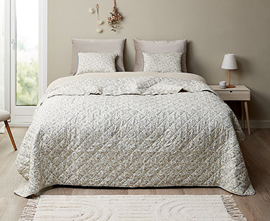 Stanza luminosa con letto rivestito da copriletto, cuscini e decorazioni tutto in tonalita beige