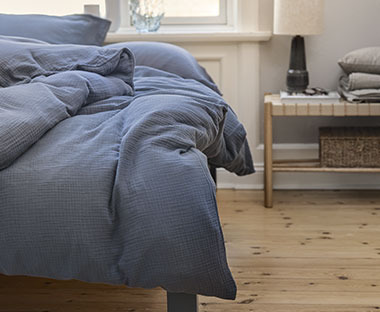 Letto in una camera da letto rustica con copriletto blu affiancato da sgabello minimal e accessori su di esso