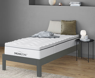 Matelas en mousse simple GOLD S100 avec de oreiller, sur un cadre de lit gris