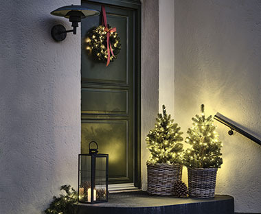 Catene di luci su piccoli alberelli di Natale all'entrata di casa vicino ad essi, diverse decorazioni natalizie