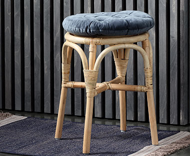 Joli tabouret en rotin naturel sur lequel est posé un coussin de chaise rond et confortable