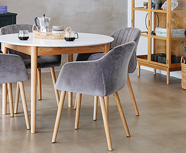 Tavolo da pranzo rotondo con gambe in legno e superficie bianca e con sedie in stoffa grigia 