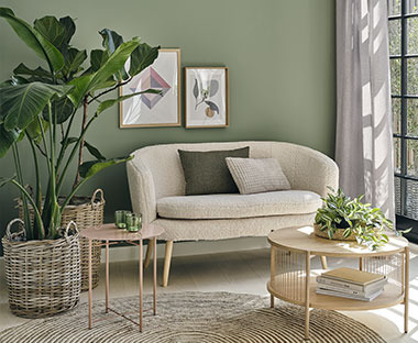 Angolo luminoso con divano color avorio abbinato a un tavolino centrale e a un tavolino in legno accanto a una pianta verde in un cesto