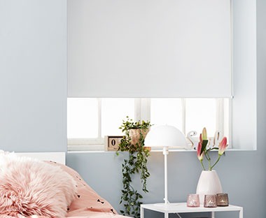 Camera da letto chiara con comodino, vaso con fiori e tenda oscurante a rullo in colore bianco