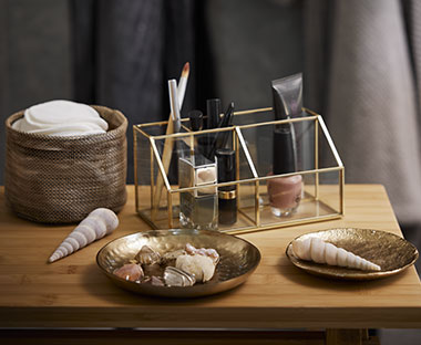 Organiseur de maquillage, boîte à bijoux et deux petits plateaux en or avec panier sur une table en bois