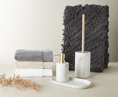 Brosse WC, distributeur de savon et plateau en métal doré, à effet marbré, complétés par trois serviettes de bain en moquette gris foncé et terreux