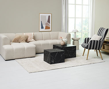 Salon clair avec un canapé beige moderne, un fauteuil à rayures et deux tables basses noires