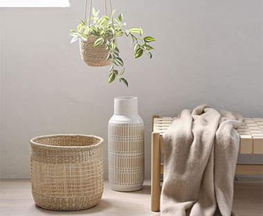 Plaid beige posé sur un banc en bois, panier en herbier marin et vase en céramique blanche