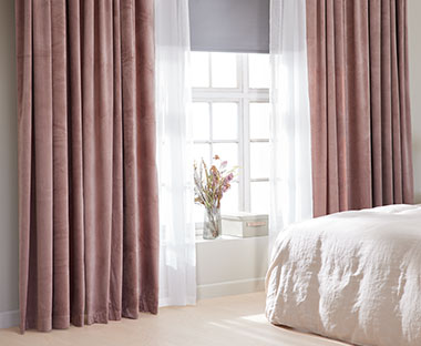 Camera da letto illuminata con letto e lenzuala bianca e tende in rosa antico 