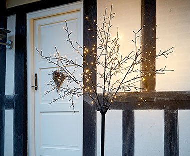 Albero di Natale con luci illumina la buia entrata di un casa bianca e nera