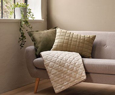 Canapé gris clair avec coussins décoratifs verts et couette beige