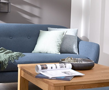Canapé en tissu bleu avec des coussins de couleur claire et table basse en bois avec un magazine