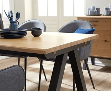 Sala da pranzo luminosa con tavolo in legno e sedie in stoffa blu e abbellita da stoviglie e candelde nere